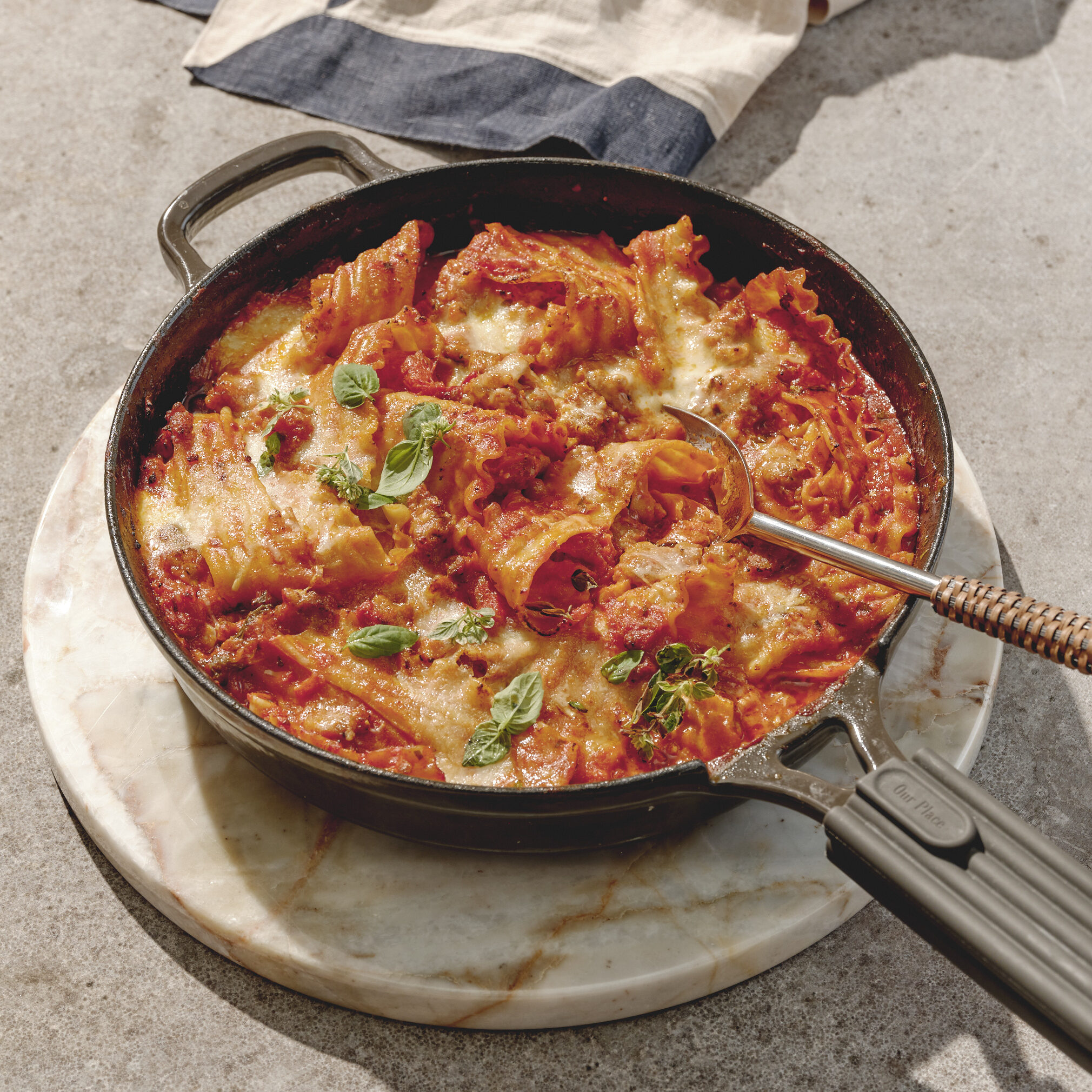 A skillet with broken lasagna pieces in a red sauce with cheese and basil.