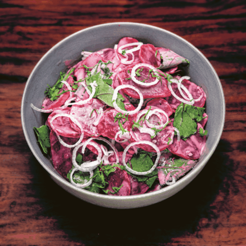 A gray bowl of beets with red onion.