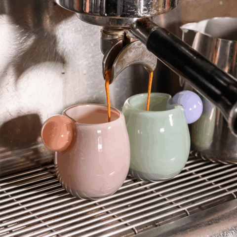 A close-up shot of two glass espresso cups under the spout of an espresso machine.