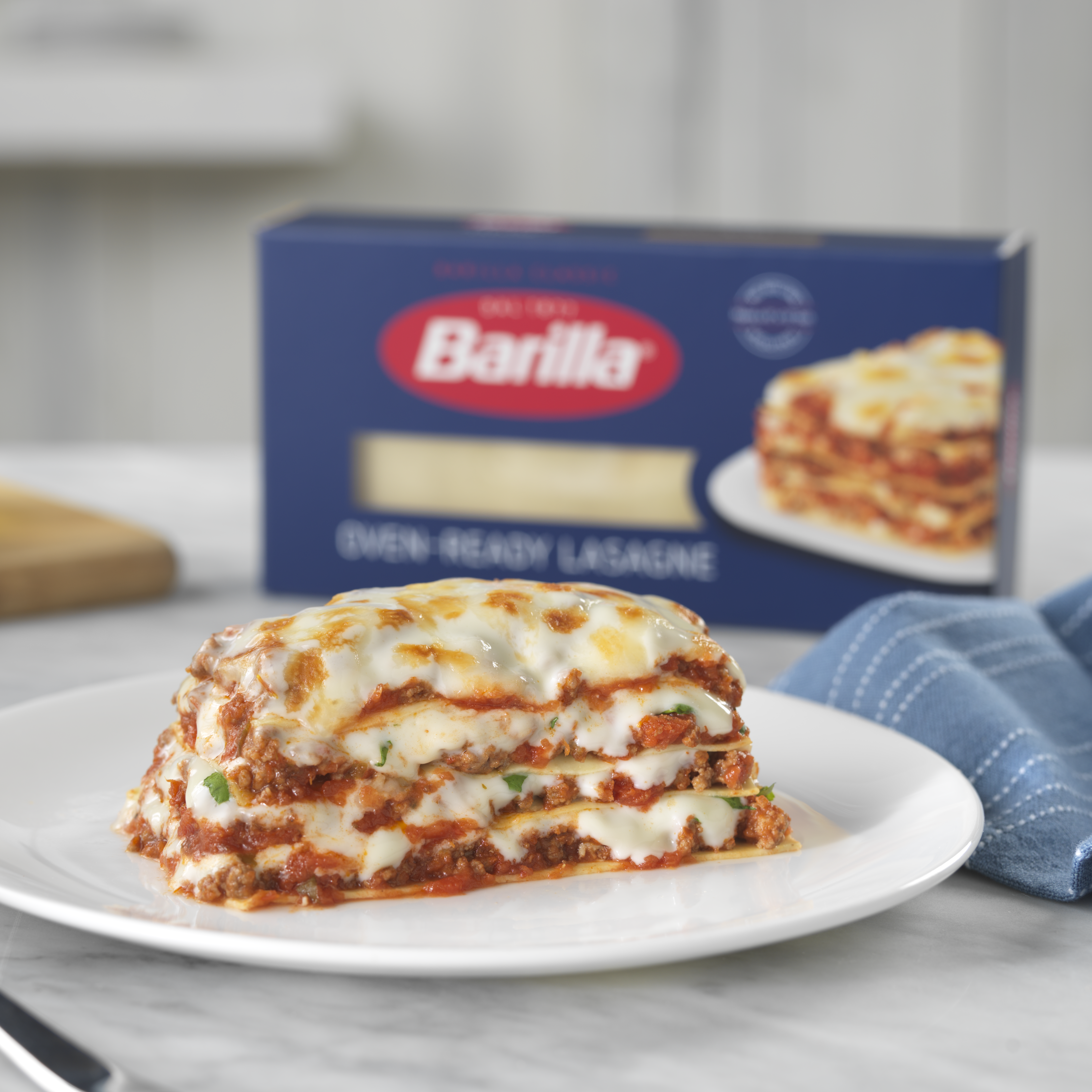 A white plate with a slice of lasagna, and a box of Barilla Lasagne Sheets in the background.
