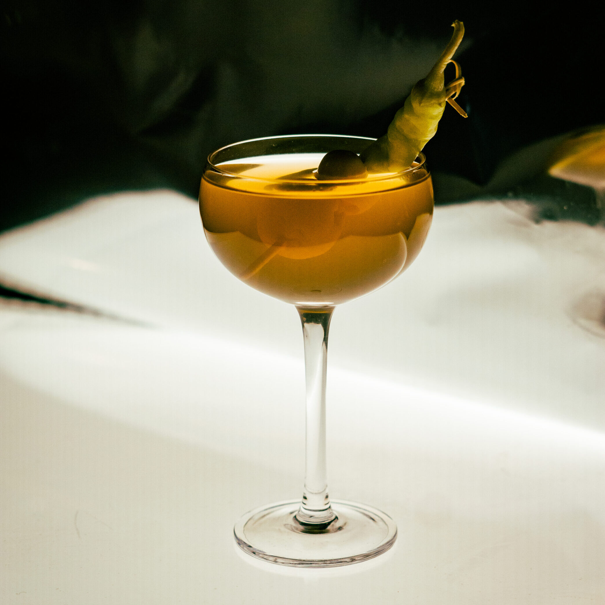 A full coupe glass garnished with a guindilla pepper.