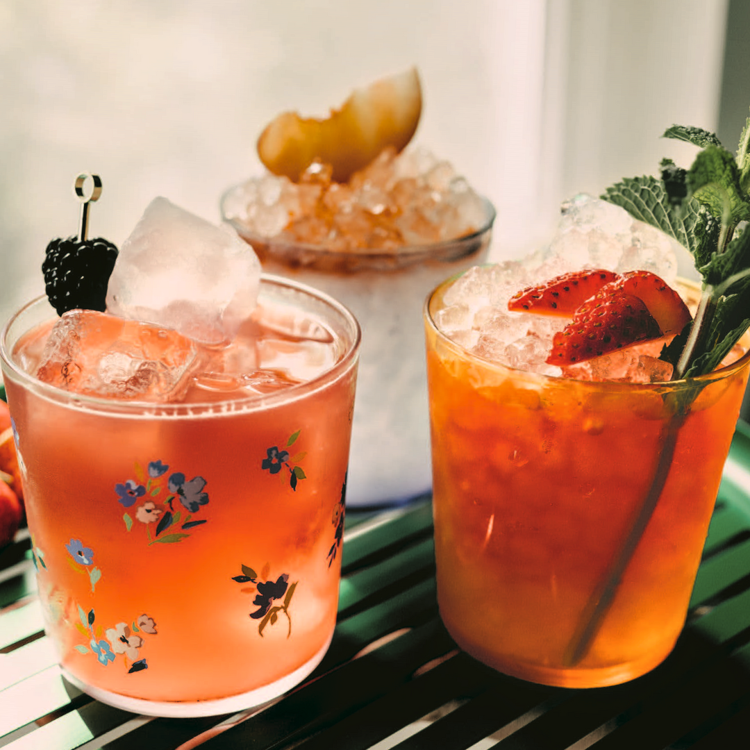 Three cocktail drinks on a green table by the window.