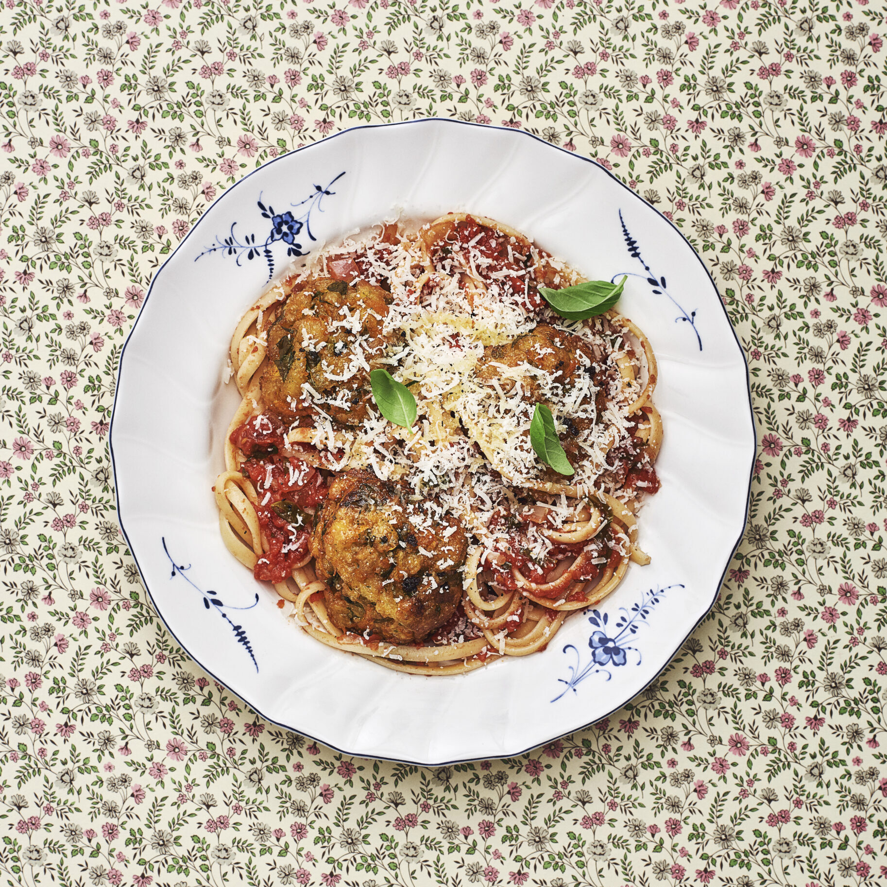 A plate with spaghetti, tomato sauce, grated parmesan and basil.