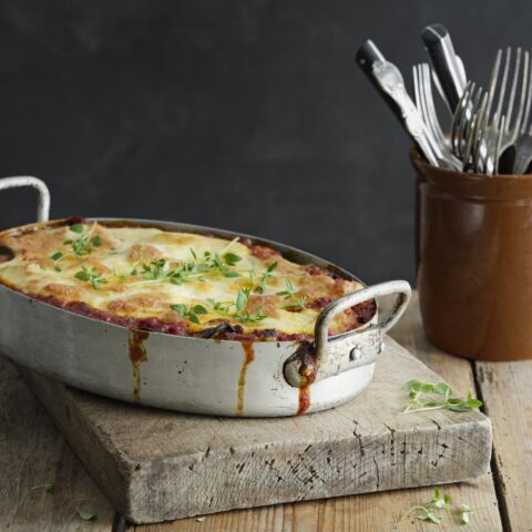 A silver dish filled with baked vegetarian lasagna next to cutlery in a holder.