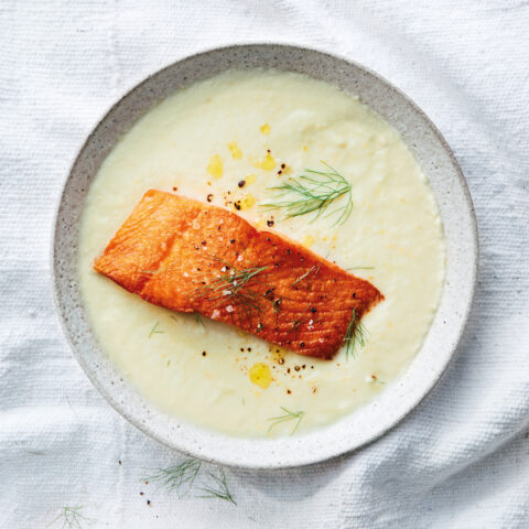 A bowl of cream-coloured soup topped with a grilled salmon fillet and fennel fronds.