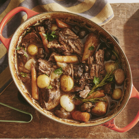 A ceramic dish with pot roast, carrots, and potatoes inside.