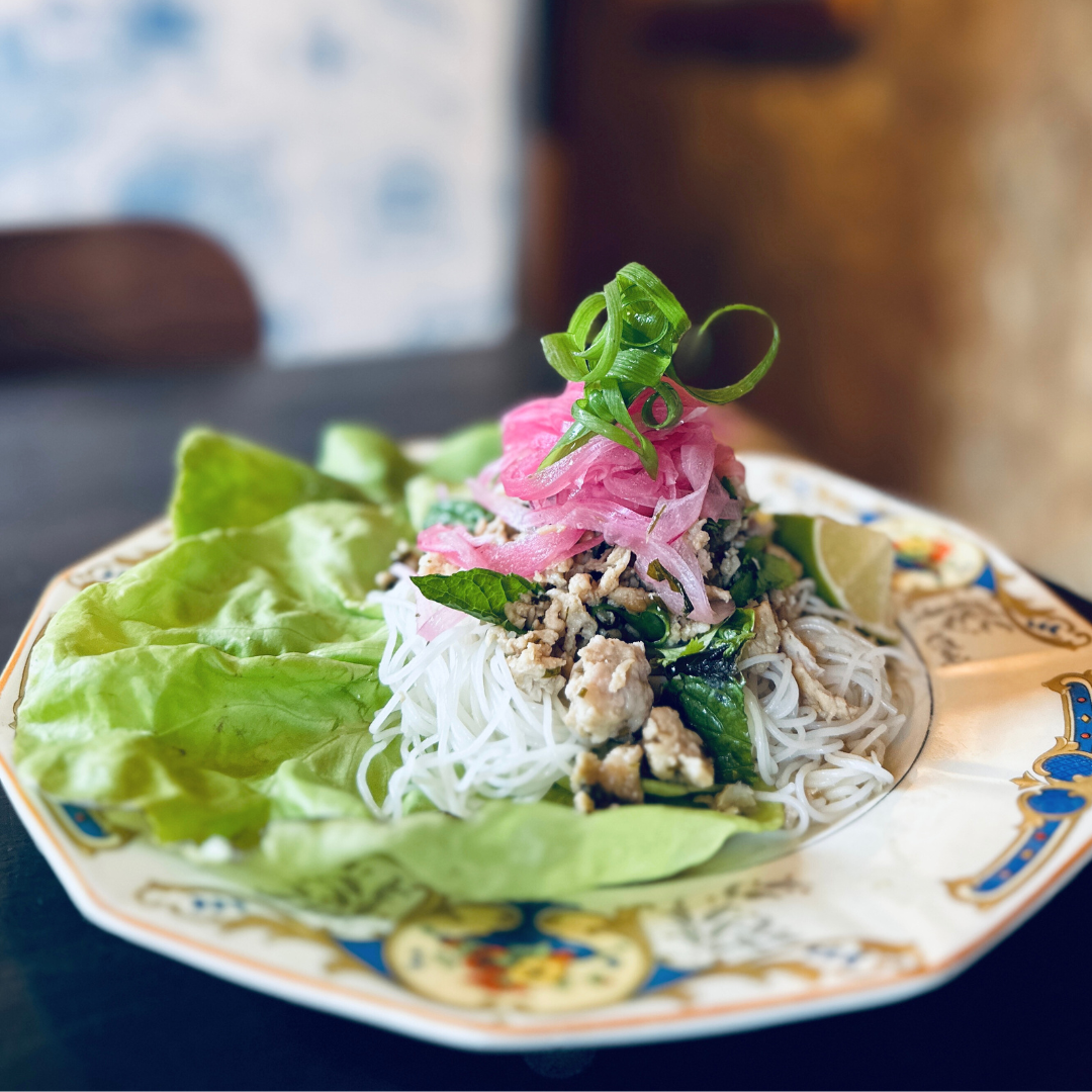 A white plate with lettuce, rice noodles and pickled onion.