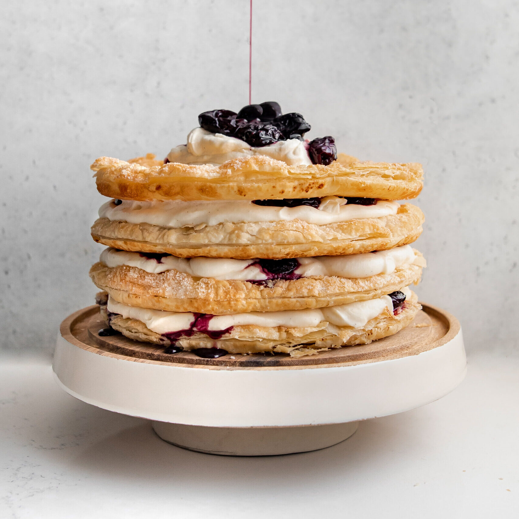 A cake on a white cake stand made from layers of puff pastry, cream and cherry compote.