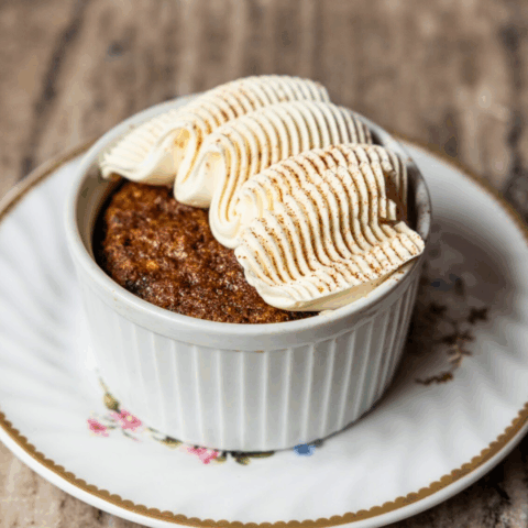 A pumpkin cake topped with piped frosting in ramekin on a floral saucer.
