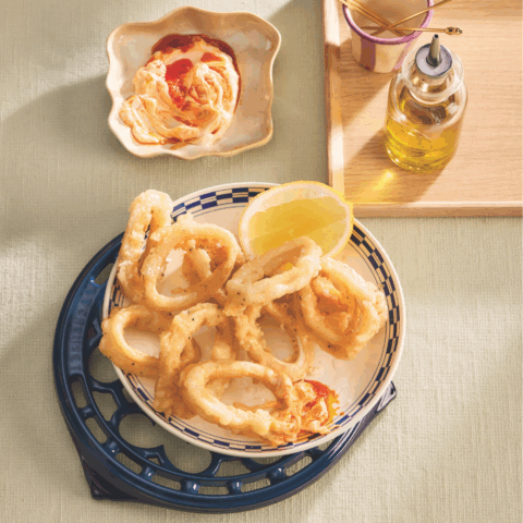 A bowl of calamari fritto misto beside a dish of calabrian chili mayo and a bottle of olive oil.