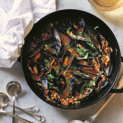 A black cast iron pan with Fregola Sarda with mussels in a tomato broth on a marble table