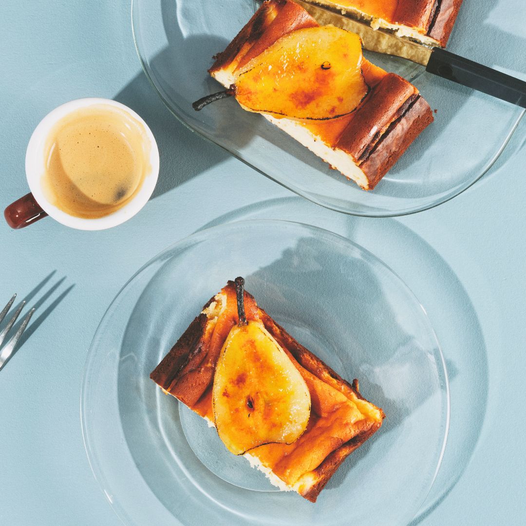 A rectangular basque cheesecake with two slices taken out and topped with poached pears.