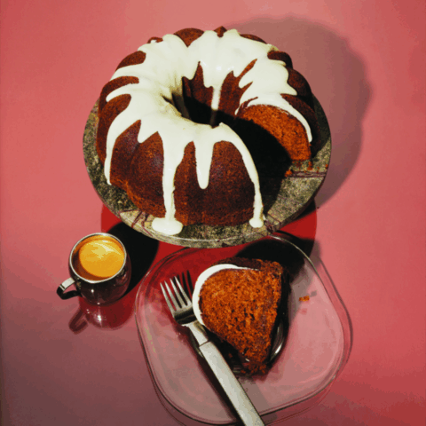 A bundt cake covered in white frosting with a slice taken out and put on a plate with a fork.
