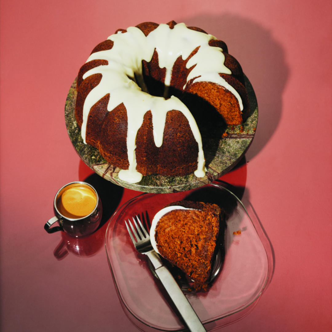 A bundt cake covered in white frosting with a slice taken out and put on a plate with a fork.