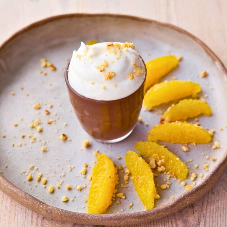 A small chocolate pot filled with Greek yogurt and chopped hazelnuts with six slices of orange on a plate.