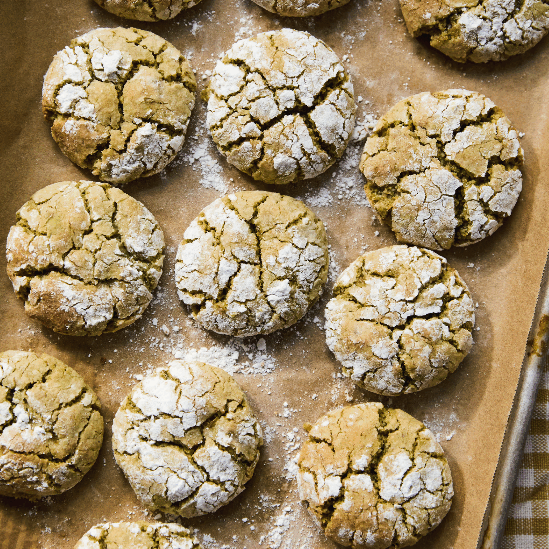 Twelve ma’akaroon cookies dusted with powdered sugar on a tray lined with parchment paper.