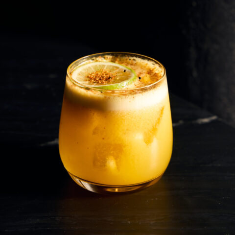 A yellow passionfruit margarita topped with a lime wheel and shichimi.