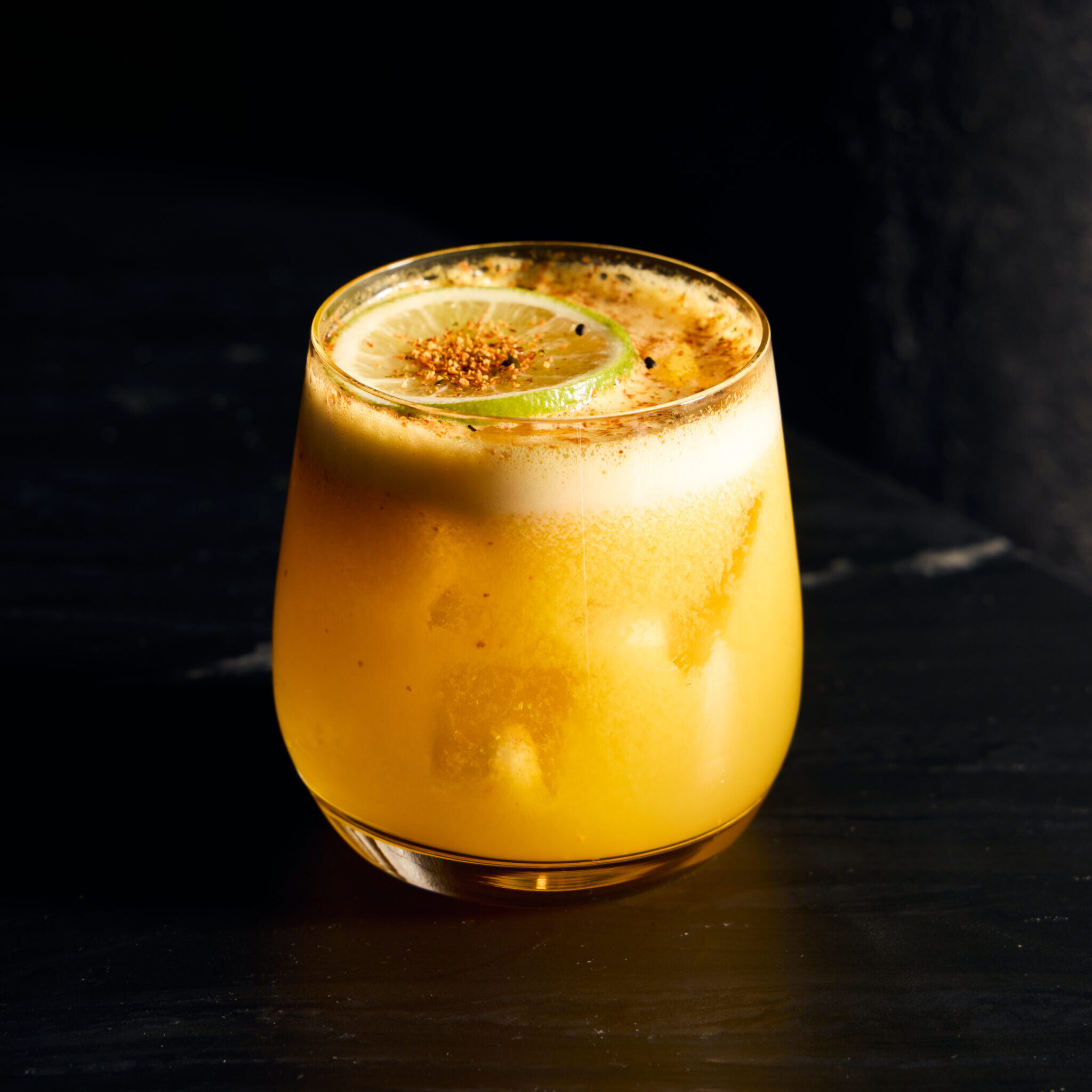 A yellow passionfruit margarita topped with a lime wheel and shichimi.