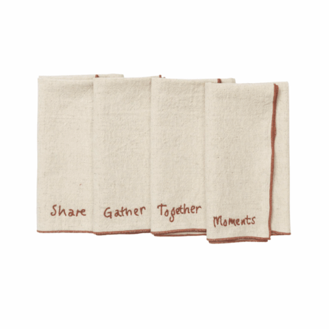 Set of four tan fabric napkins with red piping and red embroidered words.