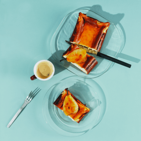 A rectangular basque cheesecake with two slices taken out and topped with poached pears.