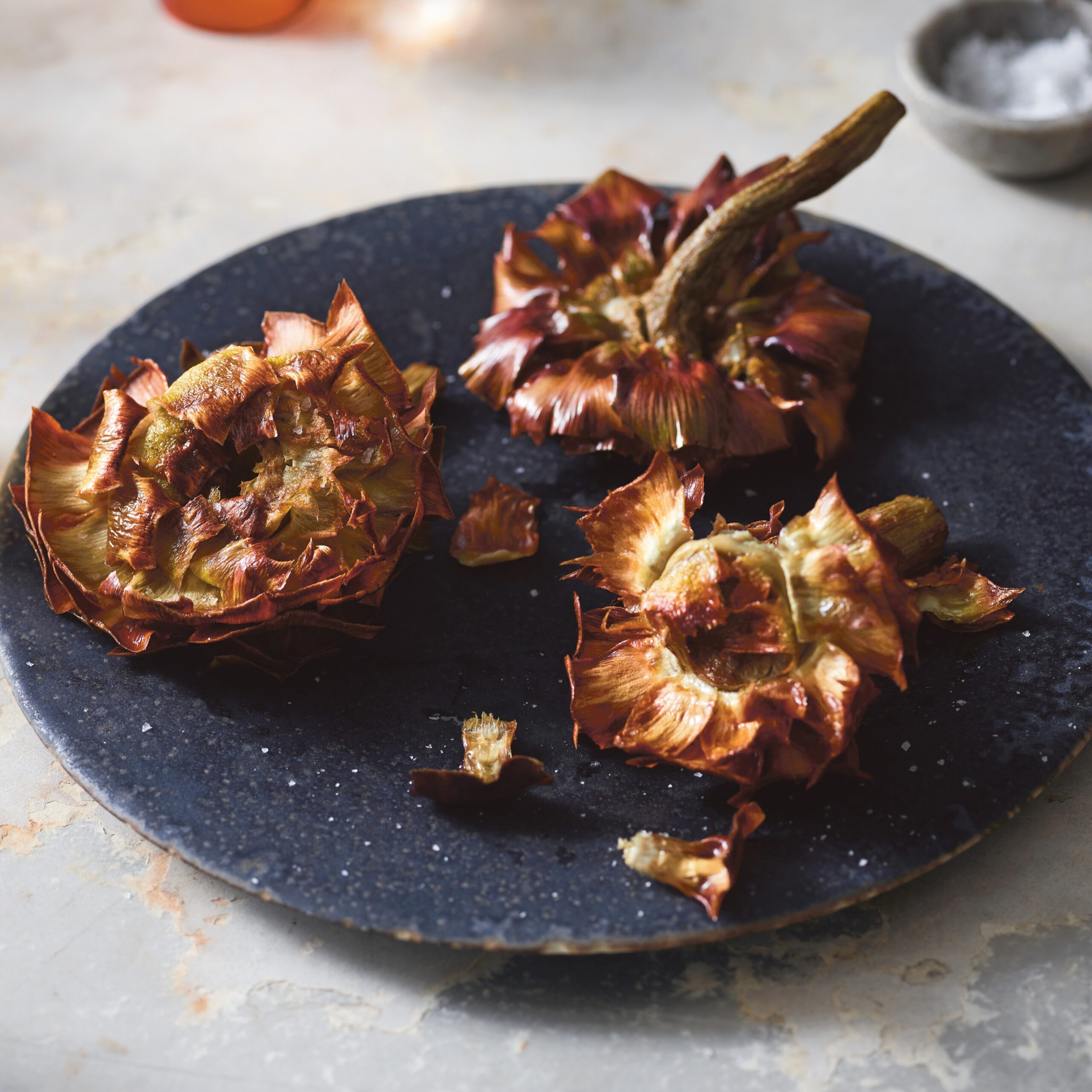 Fried artichokes on a dark blue plate on a marble counter. 