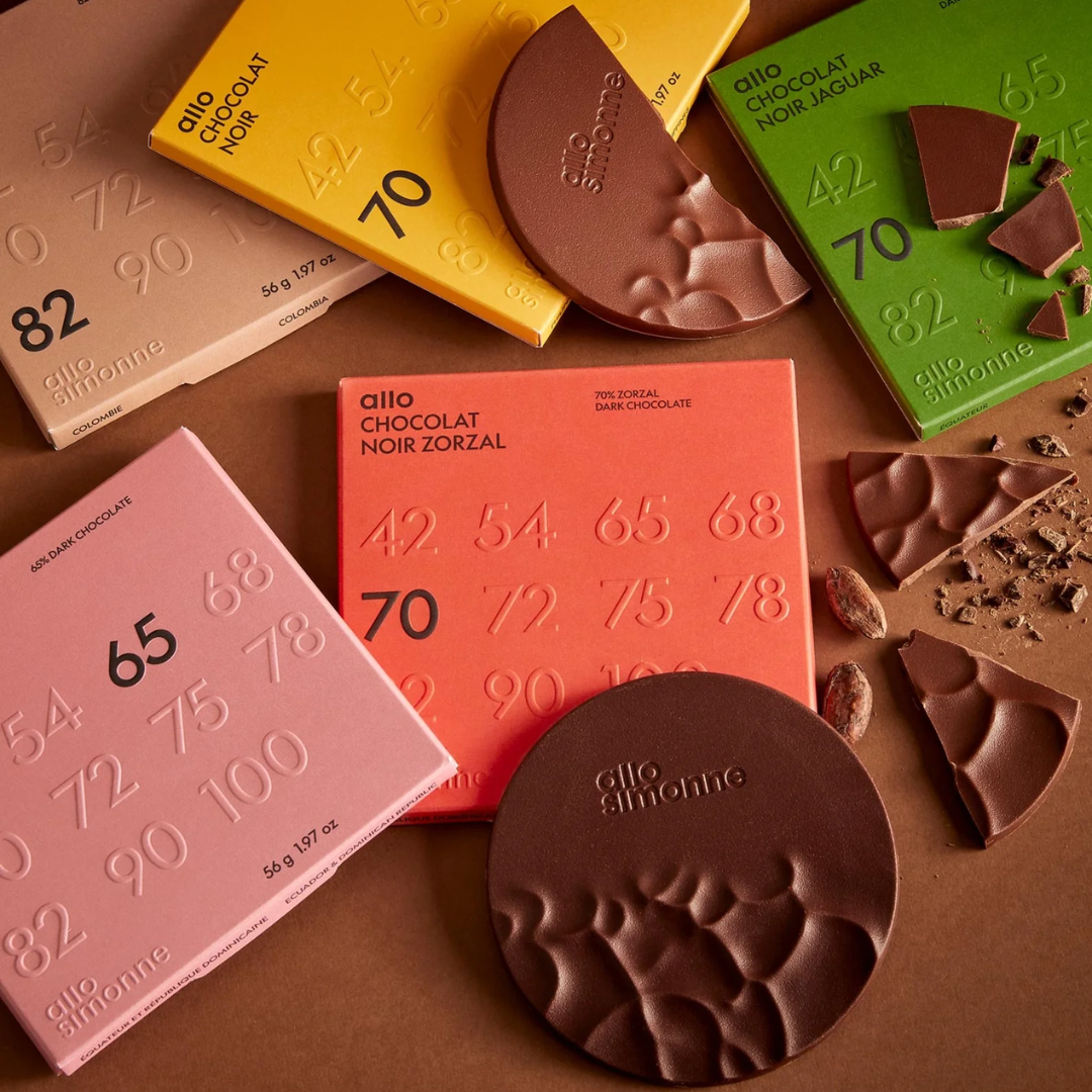 Square chocolate bar packaging and circular disks of chocolate on a brown background.