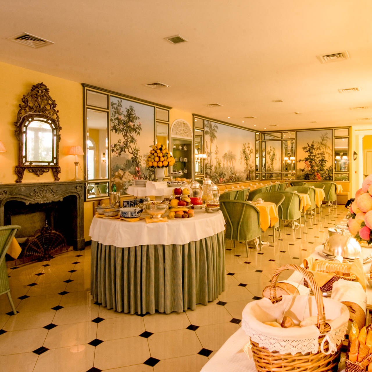 A dining room with yellow walls, grand furniture and green tablecloths.