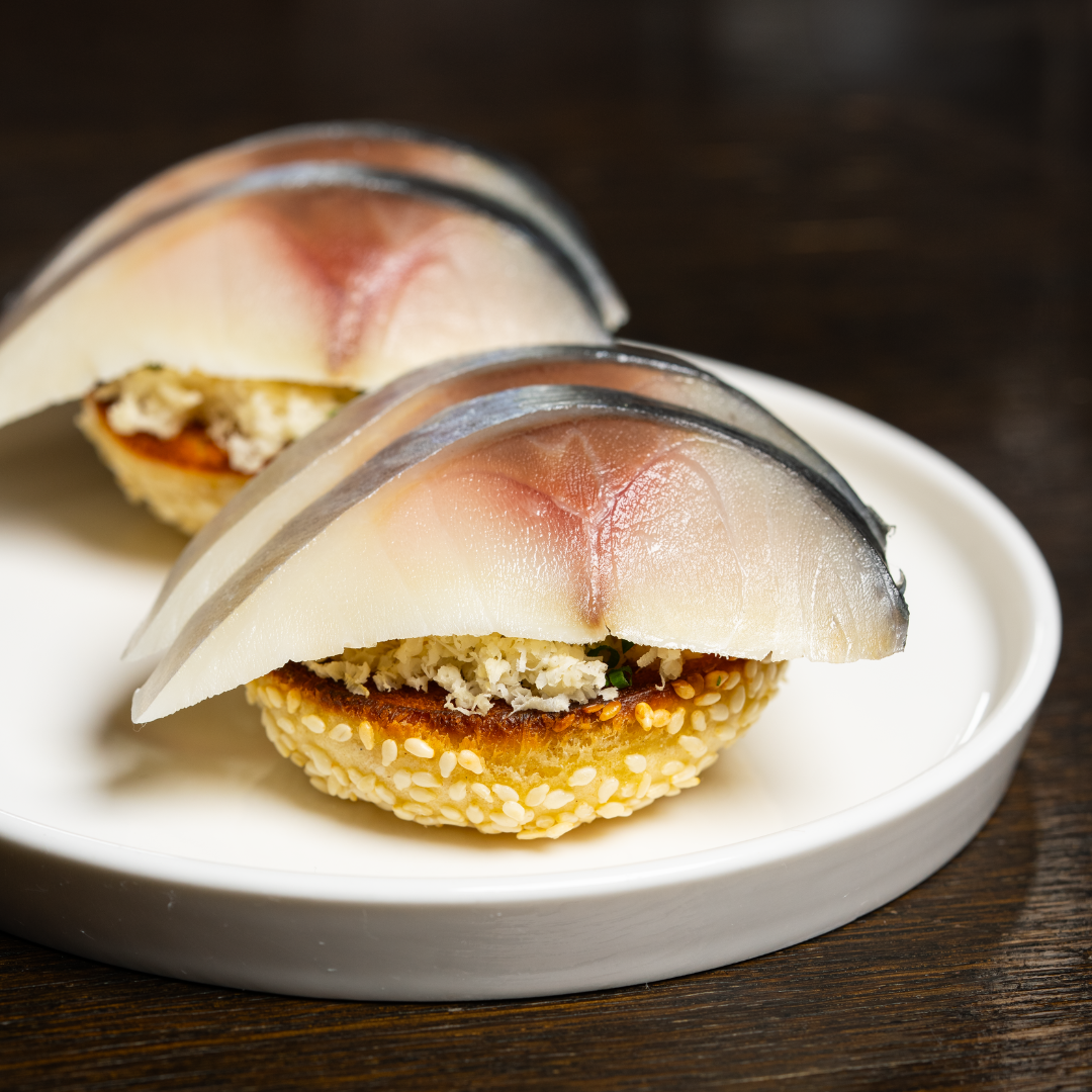 A white plate topped with two halves of a sesame ball and each topped with two slices of tuna. 