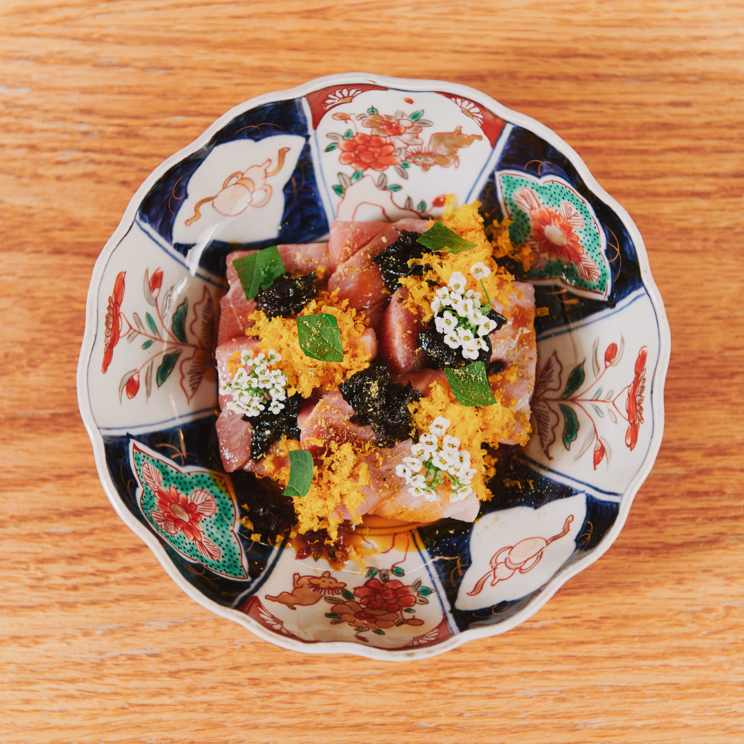 A colourful bowl filled with cubes of tuna, seaweed and white flowers. 