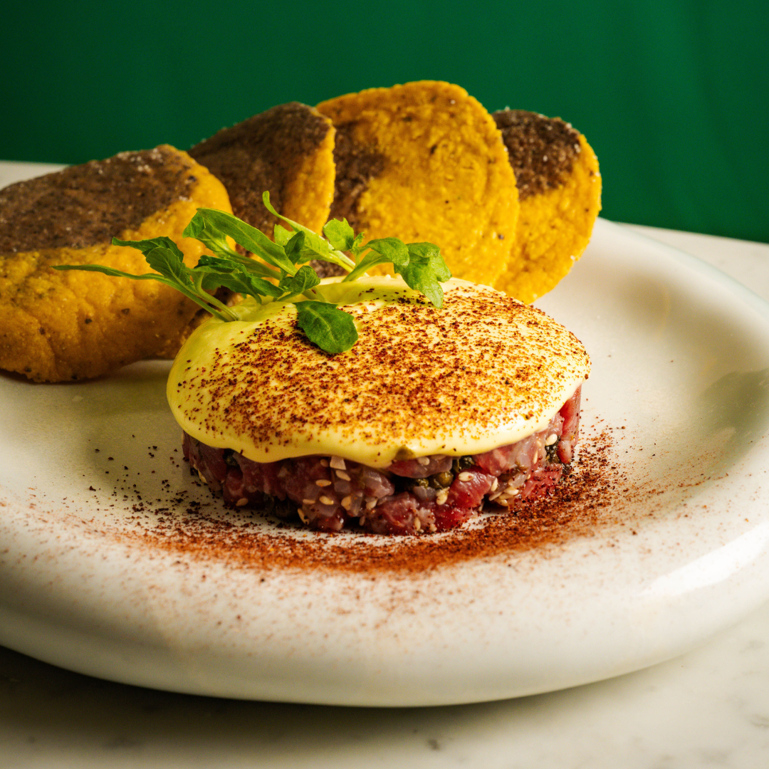 A plate with steak tartare covered in a yellow sabayon sauce and four tostadas. 