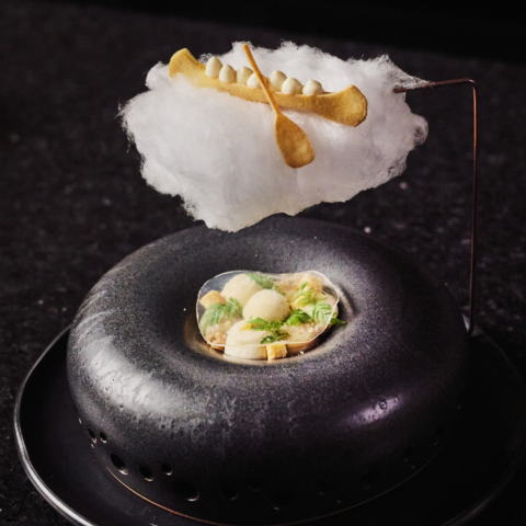 An edible mini canoe on a fluffy cloud, over a round black bowl.