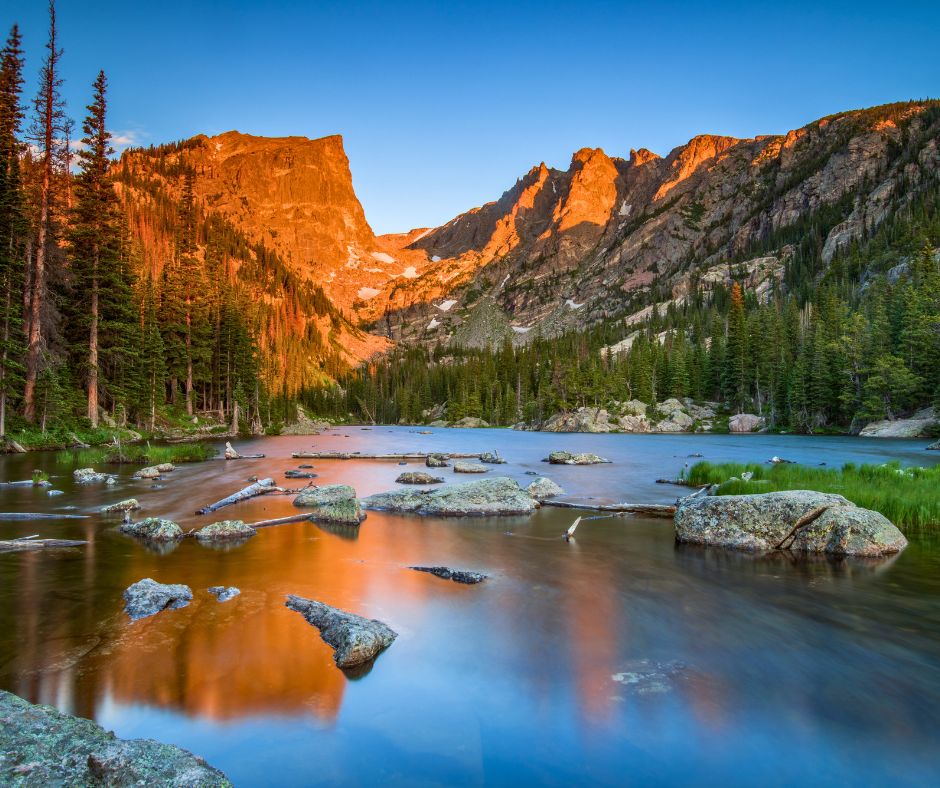 Mountain lake at sunrise reflecting rocky peaks and pine trees in Rocky Mountain National Park.