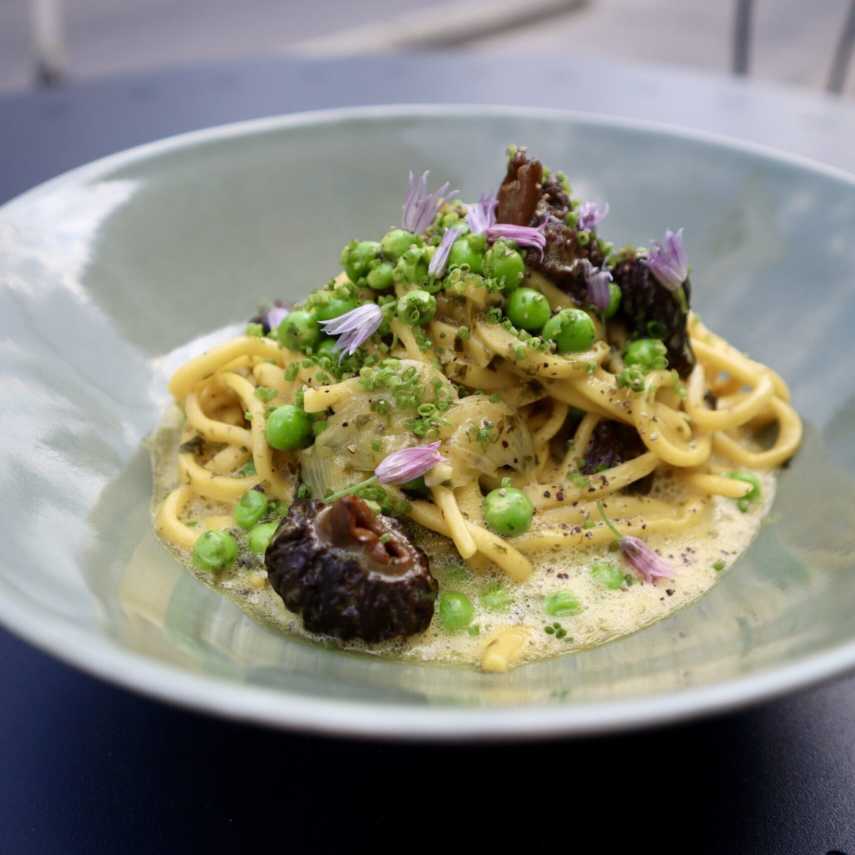 Carbonara pasta topped with peas, morels and edible purple flowers.