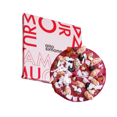 A raspberry chocolate mendiant covered in coconut shavings, almonds and dried fruits in front of a red and pink square package.