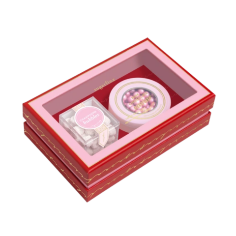 A pink and red box holding a clear cube full of white gummies and a tin of pink chocolates.