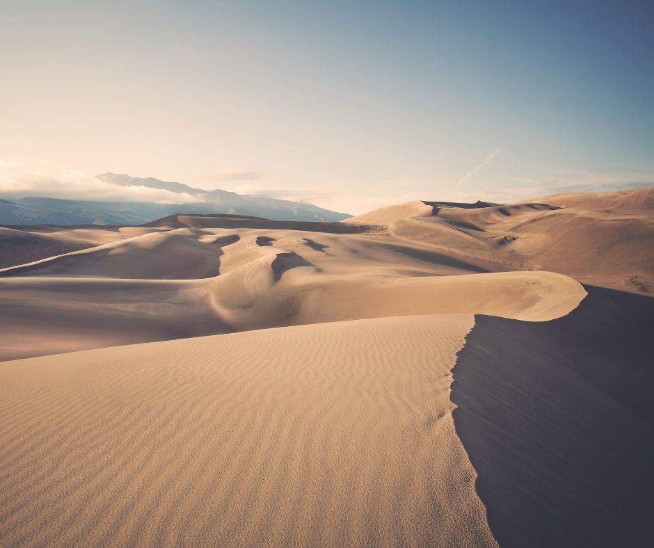 Sand dunes at sunrise with soft light and distant mountains at Great Sand Dunes National Park.