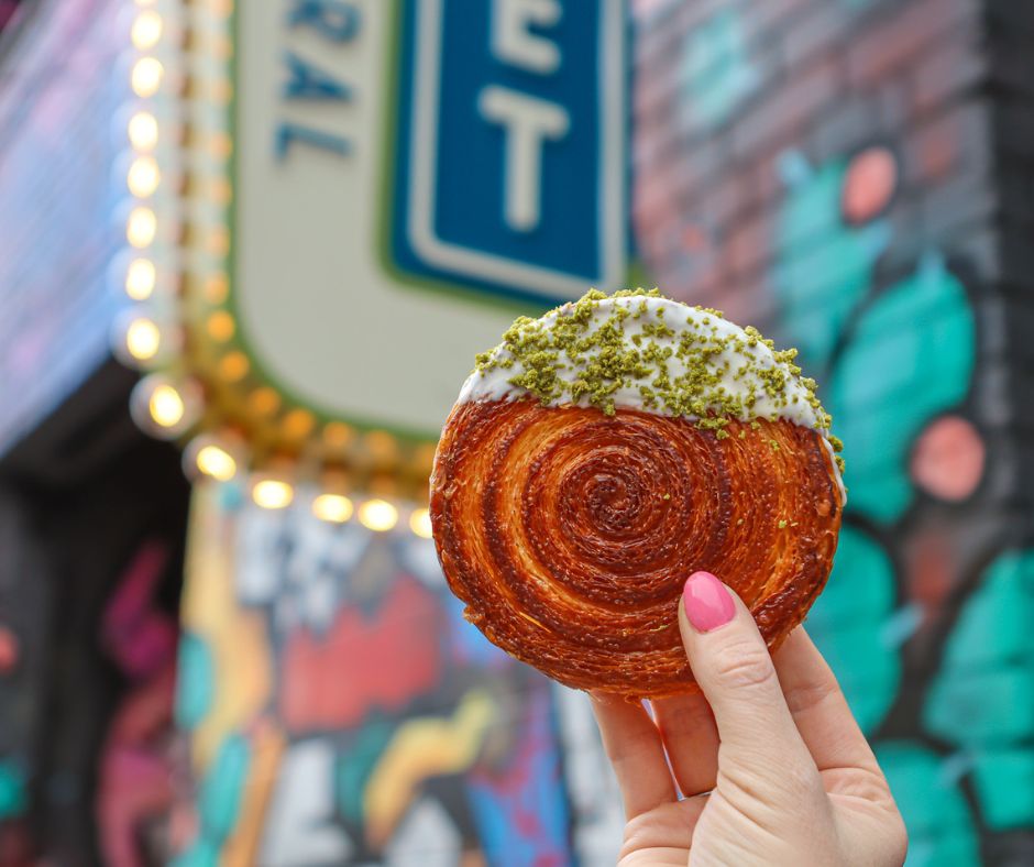 Hand holding a glazed pastry in front of colorful signage at Denver Central Market.