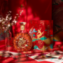 A bottle of amber-coloured XO cognac next to a decorative red box and vase of flowers on a red table.