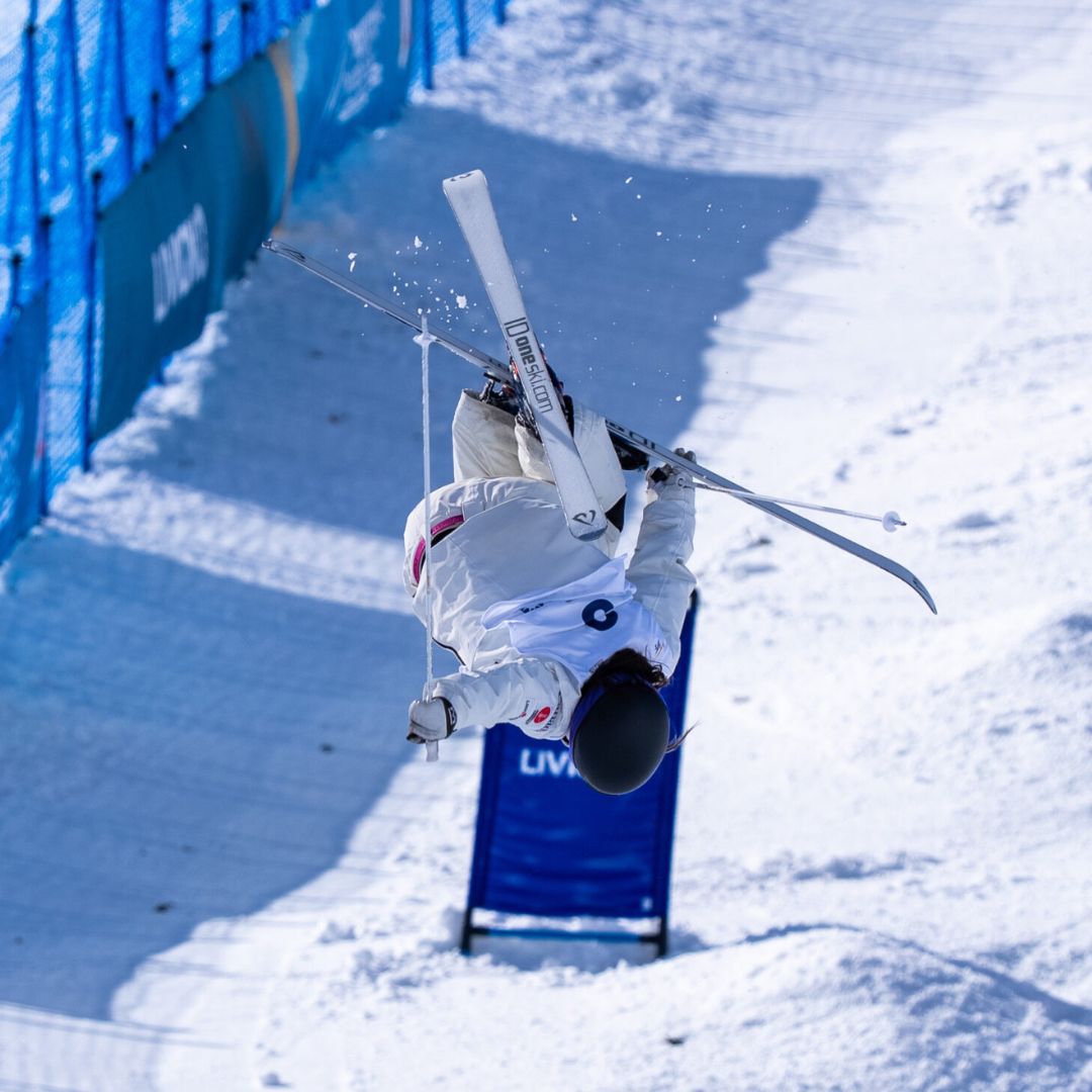 Maia-Schwinghammer-Team Canada mogul skier in a white ski suit flipping upside down.
