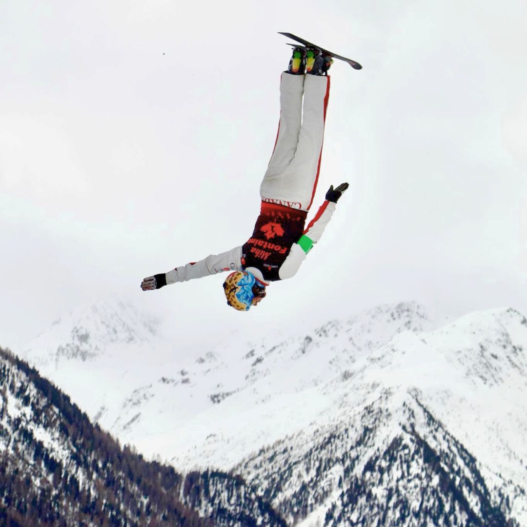 Miha Fontaine-Team-Canada-freestyle-skier flipped upside down with snowy mountains in the background.