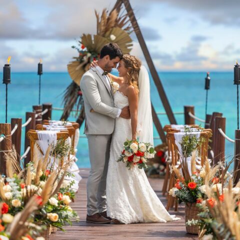Bride and groom embracing during a beachfront destination wedding ceremony over turquoise ocean waters