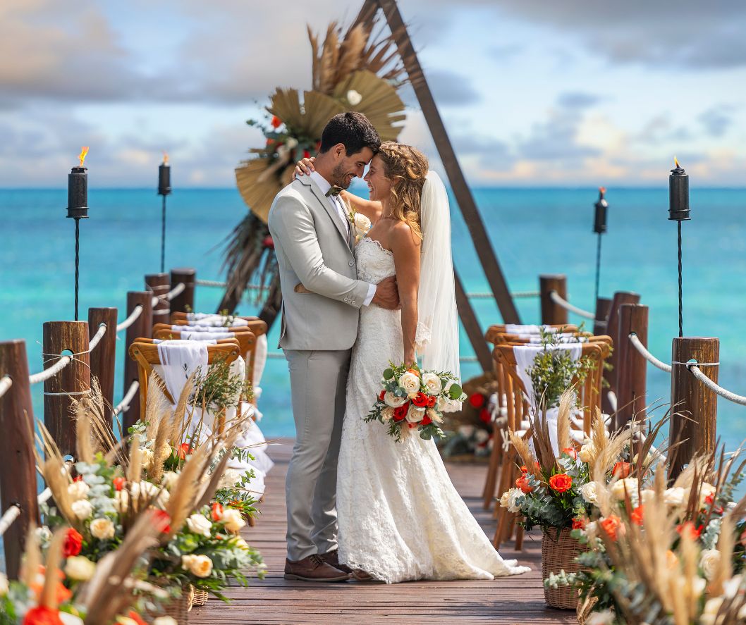 Bride and groom embracing during a beachfront destination wedding ceremony over turquoise ocean waters