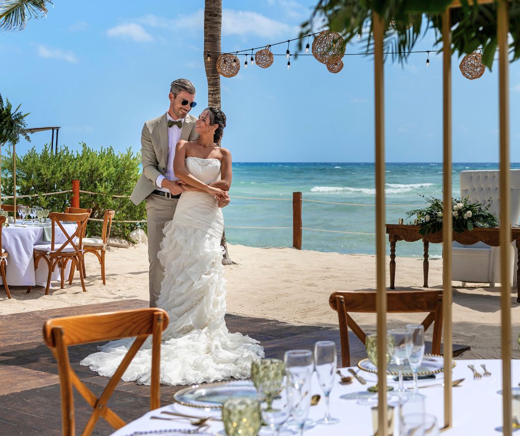 Newlyweds walking along a beach reception setup with ocean views during a destination wedding celebration