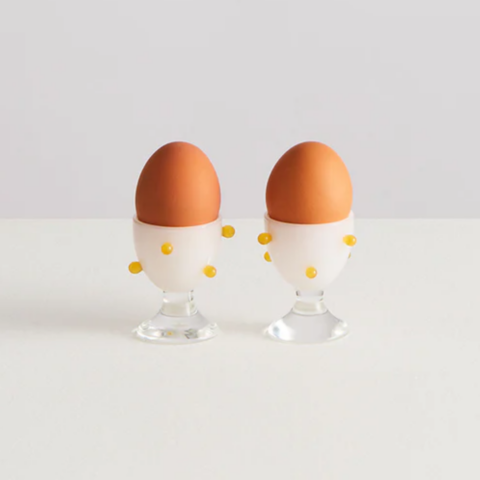 Two brown eggs in white glass egg cups with yellow 3D dots.