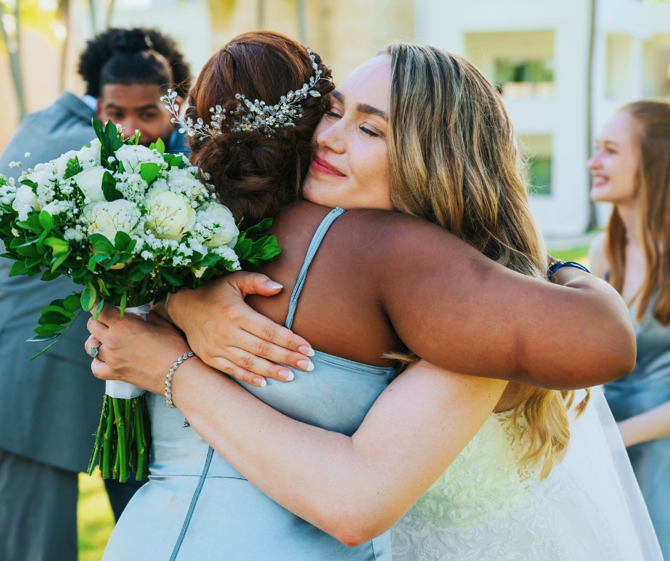 Bride hugging a guest while holding a bouquet during an outdoor wedding celebration.