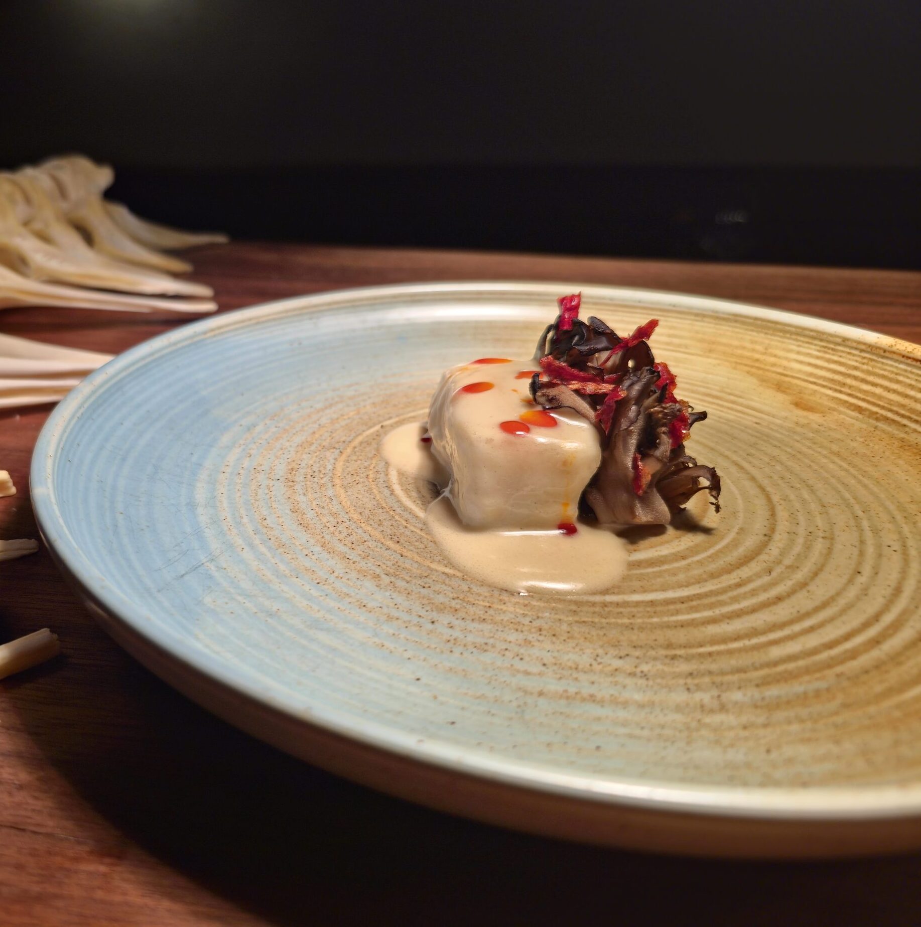A piece of halibut topped with a white sauce next to maitake mushroom.