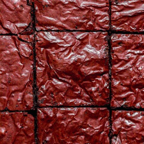 Overhead view of red velvet brownies with a glossy, crinkled top cut into squares