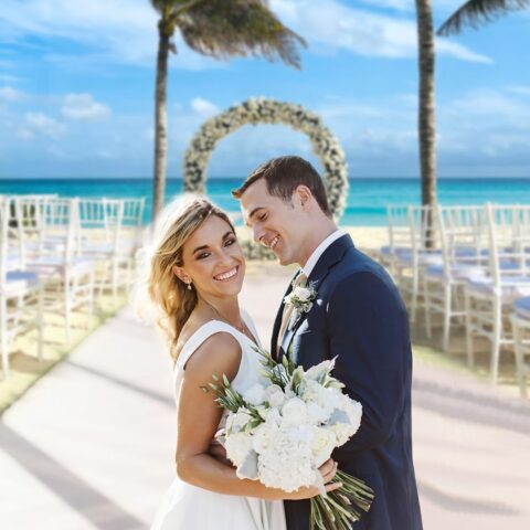 Bride and groom posing at a beachfront destination wedding ceremony with ocean view and floral arch