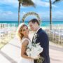Bride and groom posing at a beachfront destination wedding ceremony with ocean view and floral arch