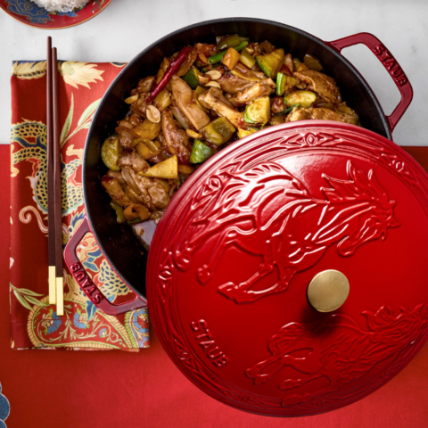 A red cast iron pot with horse enamel design on the lid opened to show stir-fried veggies.